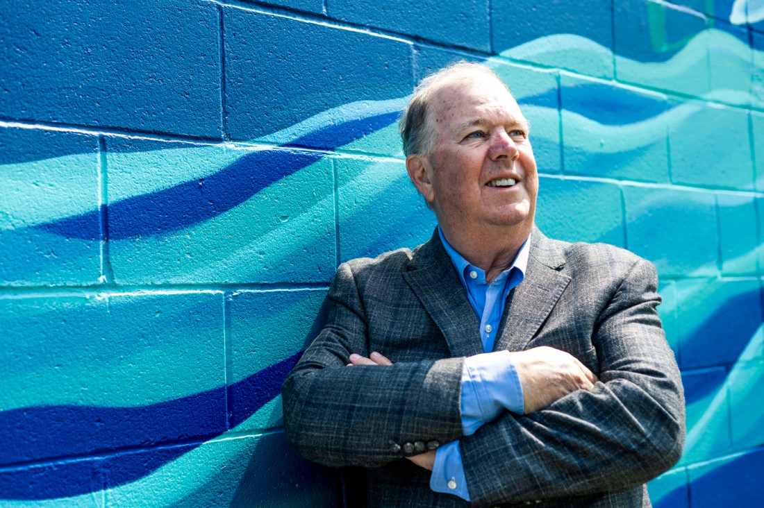 Headshot of Alan McKim, standing in front of a mural painted like water.