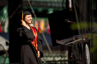 Clara Wu standing at speaker podium in cap and gown