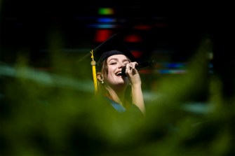 Person singing national anthem in graduation cap and gown