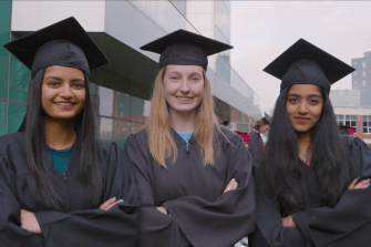 Three graduating seniors in their commencement regalia, posing and ready to dance.