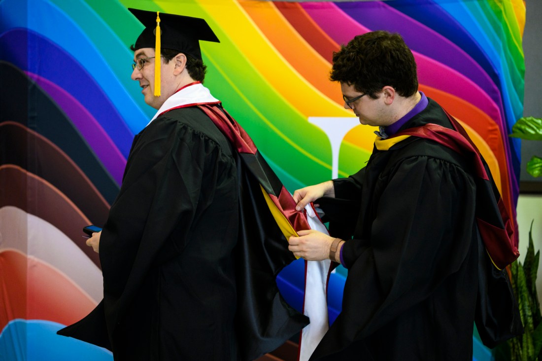 Northeastern graduate helping another graduate with their cap and gown. 