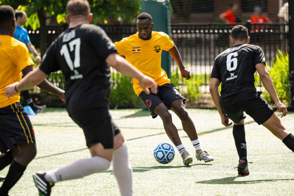 Multiple players run after a soccer ball on a grass-covered field.