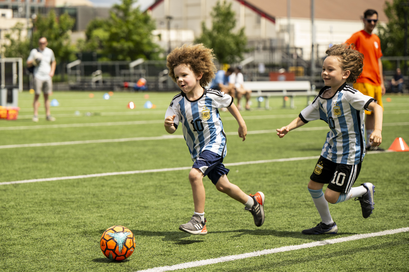 Two children run after a soccer ball on a grass-covered field. 