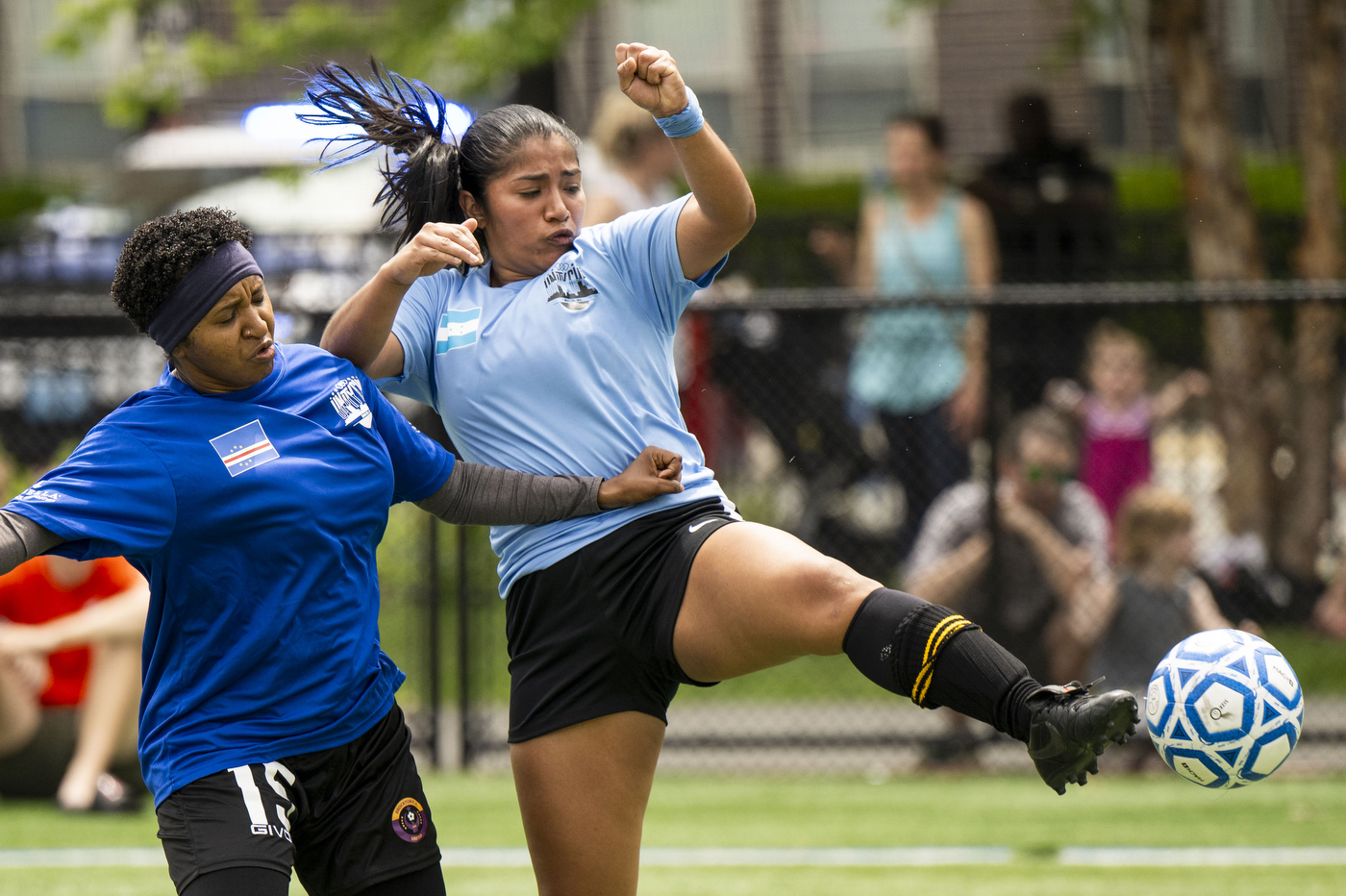 Two players run after a soccer ball on a grass-covered field. 