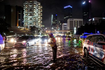 A man walks in shallow water flooding Jakarta