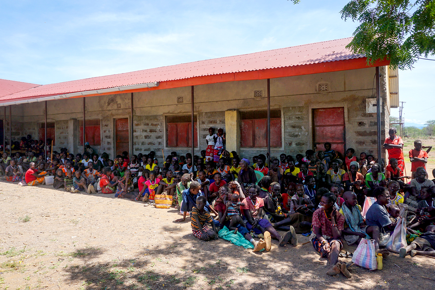 Hundreds of people sit in front of a building with a red roof. 