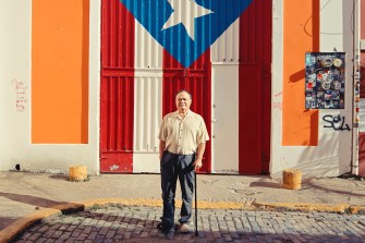 A person stands in front of the flag of Puerto Rico.