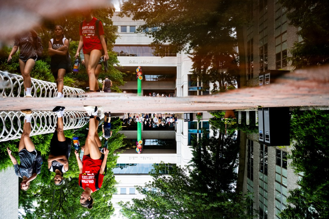 Northeastern community members walking on campus, reflected in a puddle. 