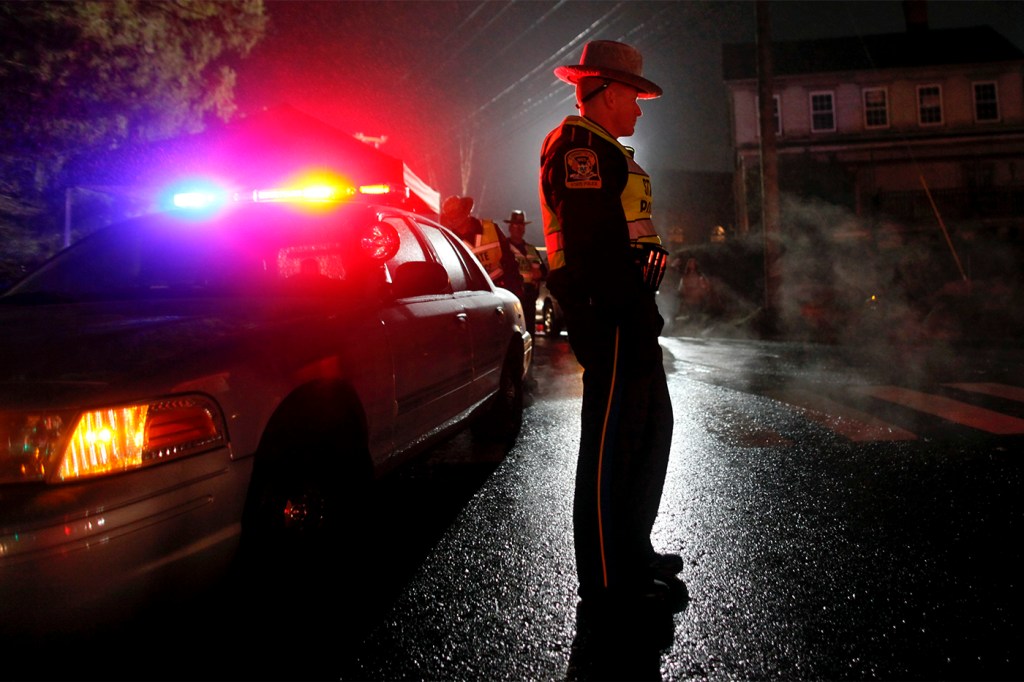 CT state trooper standing outside a police car at night in Newtown, CT