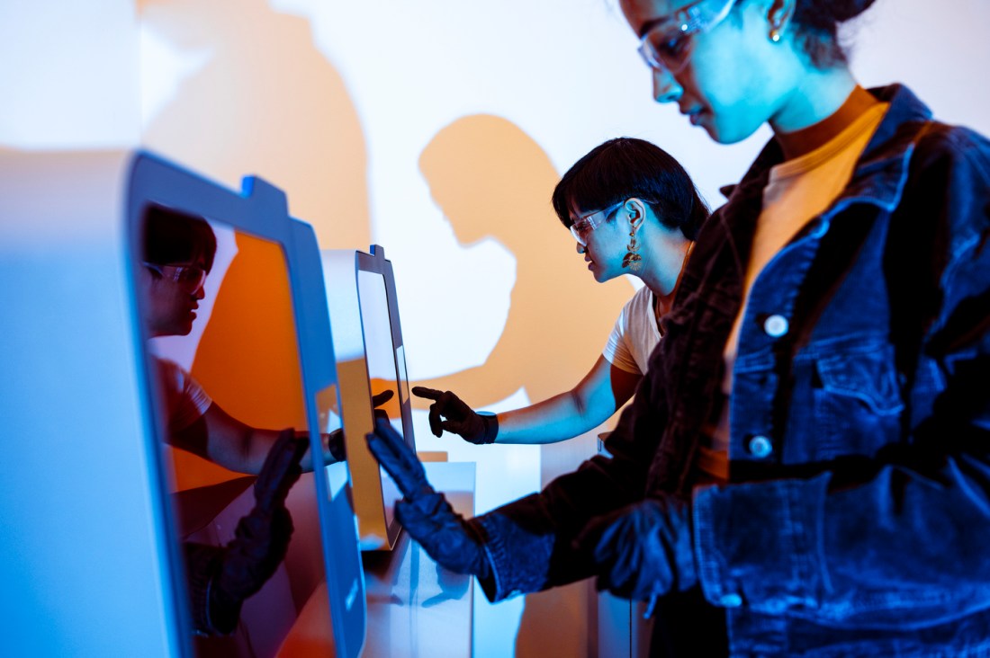 Northeastern community members wearing goggles and gloves using a touchscreen. 