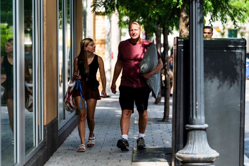 two people walking, one carrying a bag and the other carrying a pillow