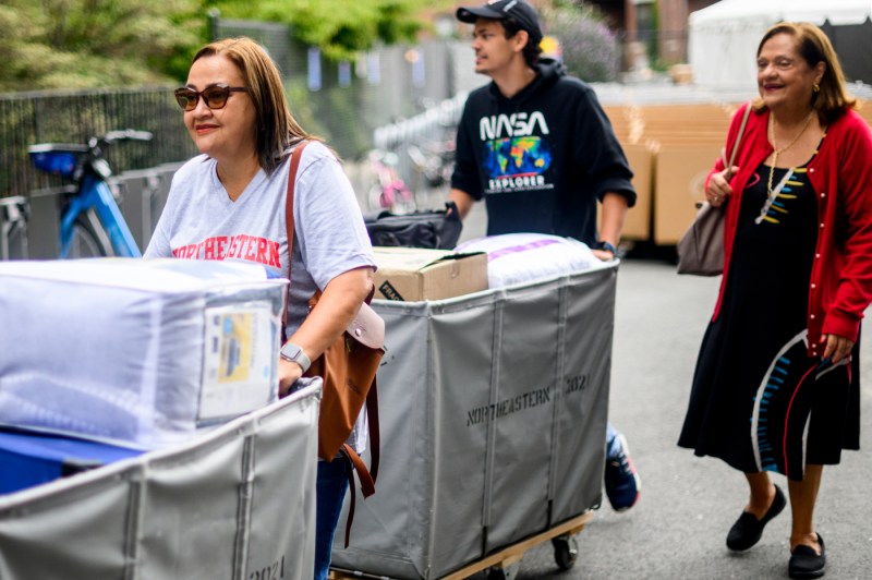 students and family members pushing wheeled carts of their belongings