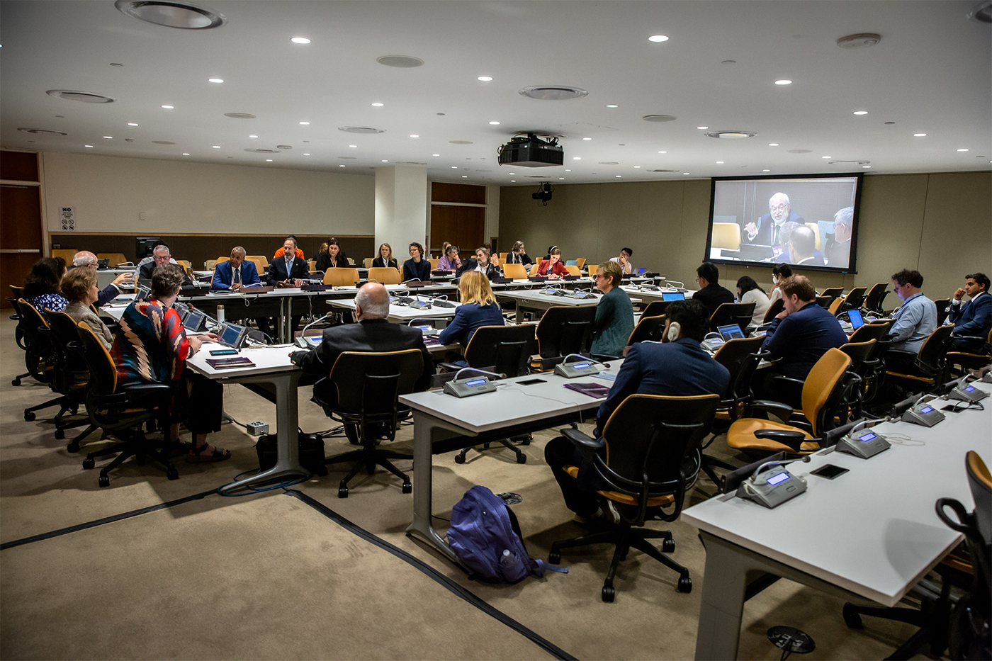 conference room full of people, with a projector displaying a person speaking