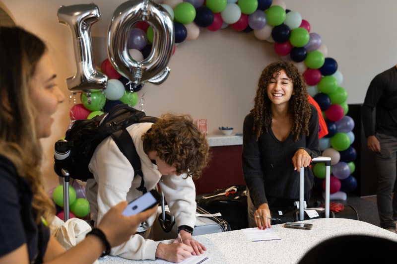 People laugh while standing near multi-colored balloons. 