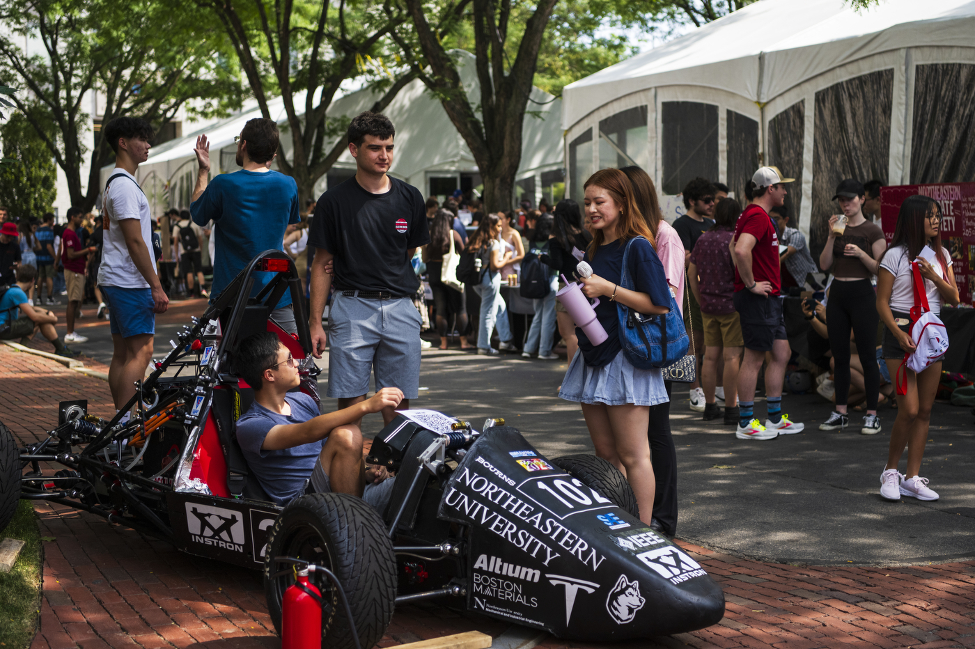 People talk to a person sitting inside a race car at Fall Fest.