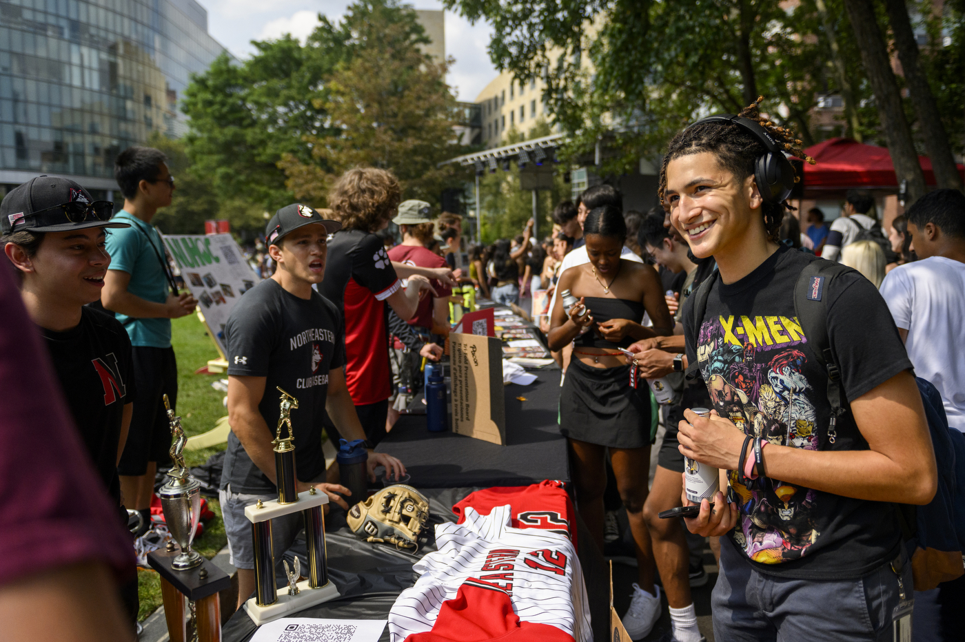 A person smiles while talking to people standing in front of a table outside.