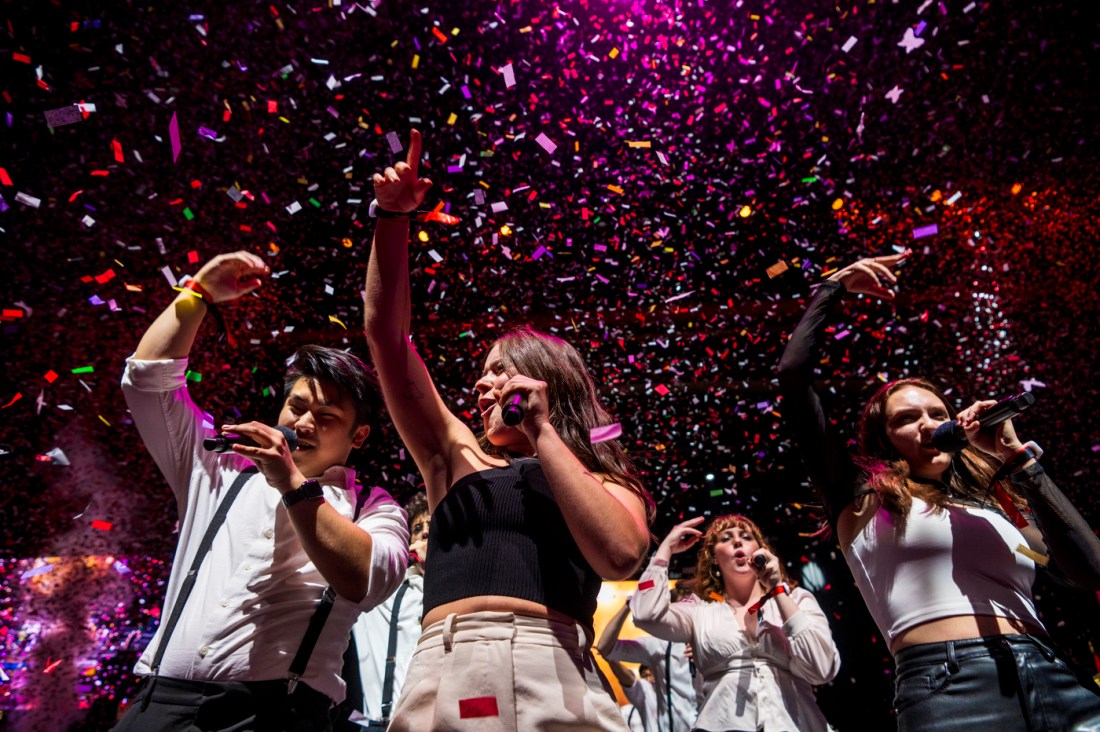 Confetti falling over Northeastern community members singing into microphones.