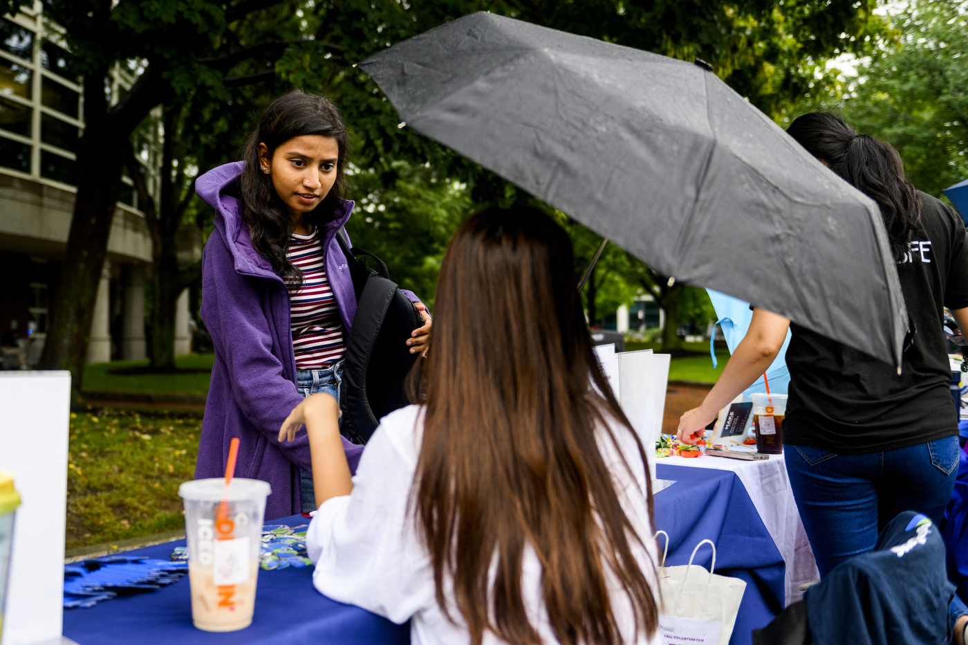 Student walking in the rain underneath a black umbrella.