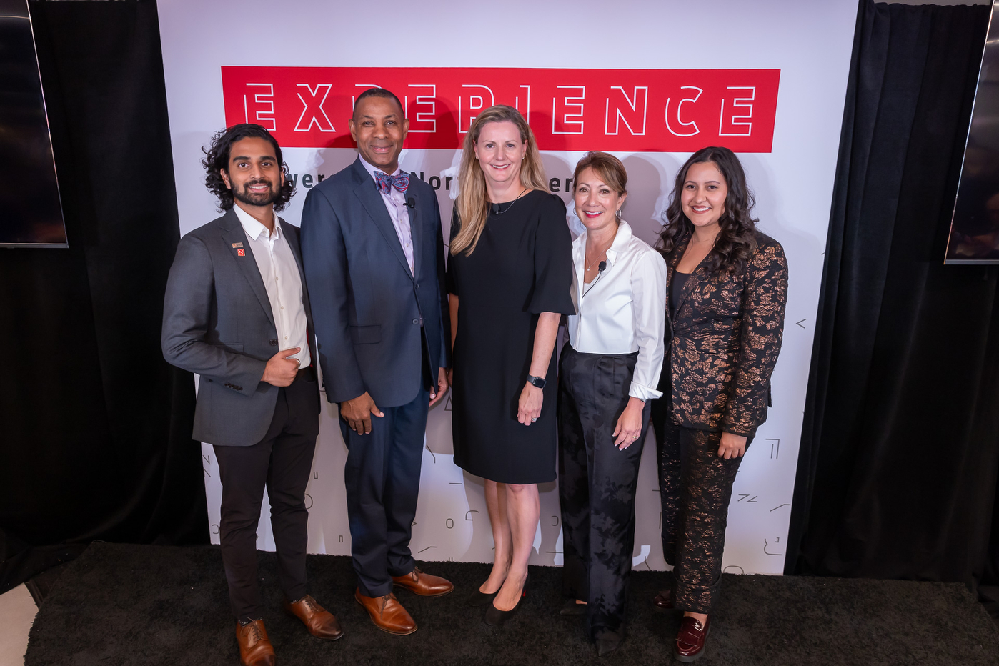 Group posing for photo in front of Experience backdrop. 