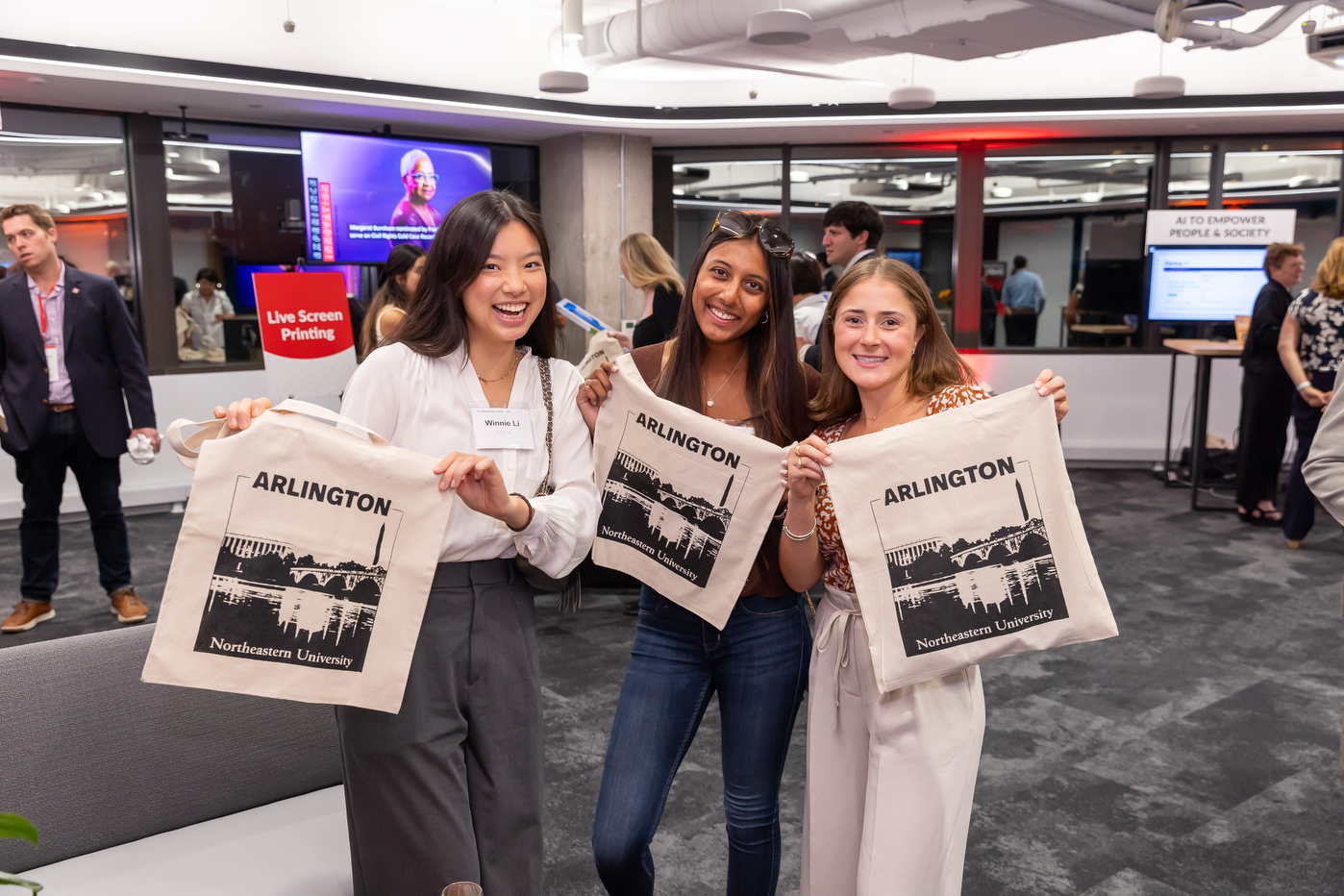 Three people posing with Northeastern University Arlington tote bags.