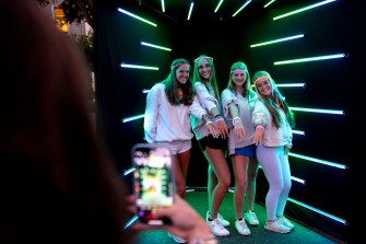Four students pose in front of a glowing backdrop while showing off glowsticks. Another student takes their photo.