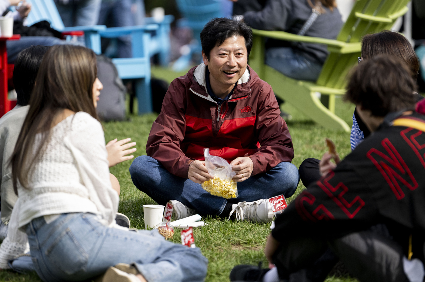 People sitting cross legged on the grass at Family and Friends weekend.