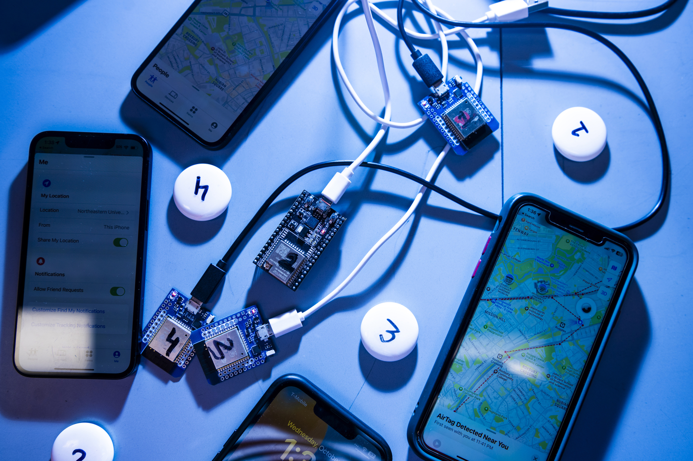 3 iPhones and 3 air tags on a table with various cords. 