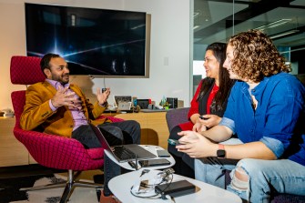 Aanjhan Ranganathan sitting in a chair talking with two students about AirTag research.