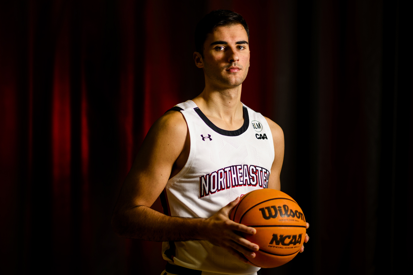 Luka Sakota posing for a headshot while wearing a Northeastern jersey and holding a basketball.