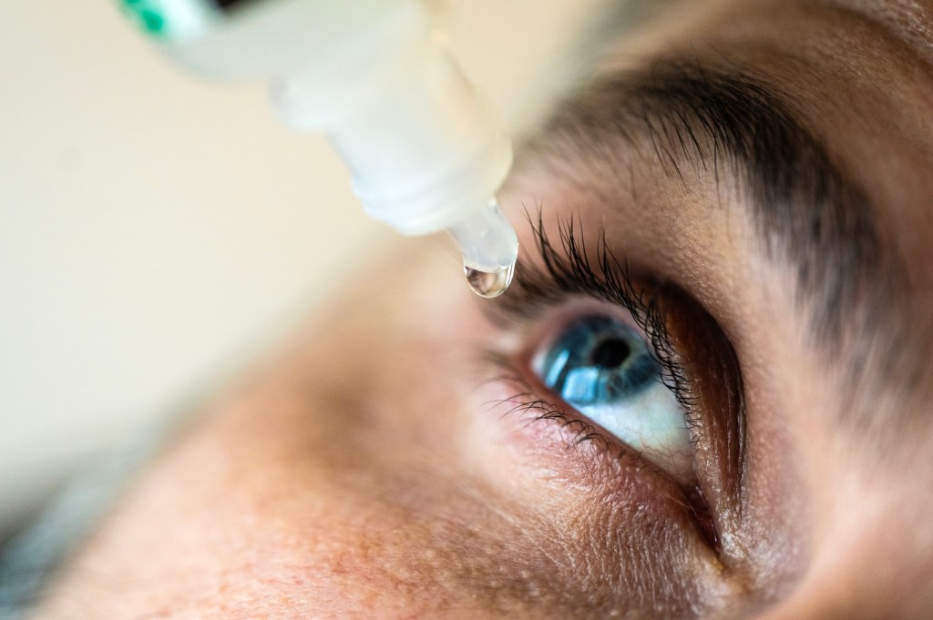 Person with blue eyes using eyedrops.