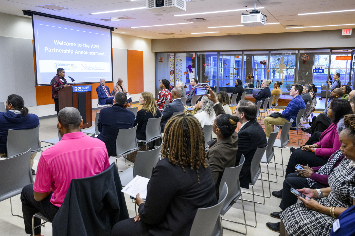 Speaker at a podium in front of a room full of people at the A2M Partnership Announcement between Northeastern University and Roxbury College.