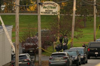 Law enforcement officers standing next to yellow caution tape strung between two light posts under the Schemengee's Bar and Grille sign.