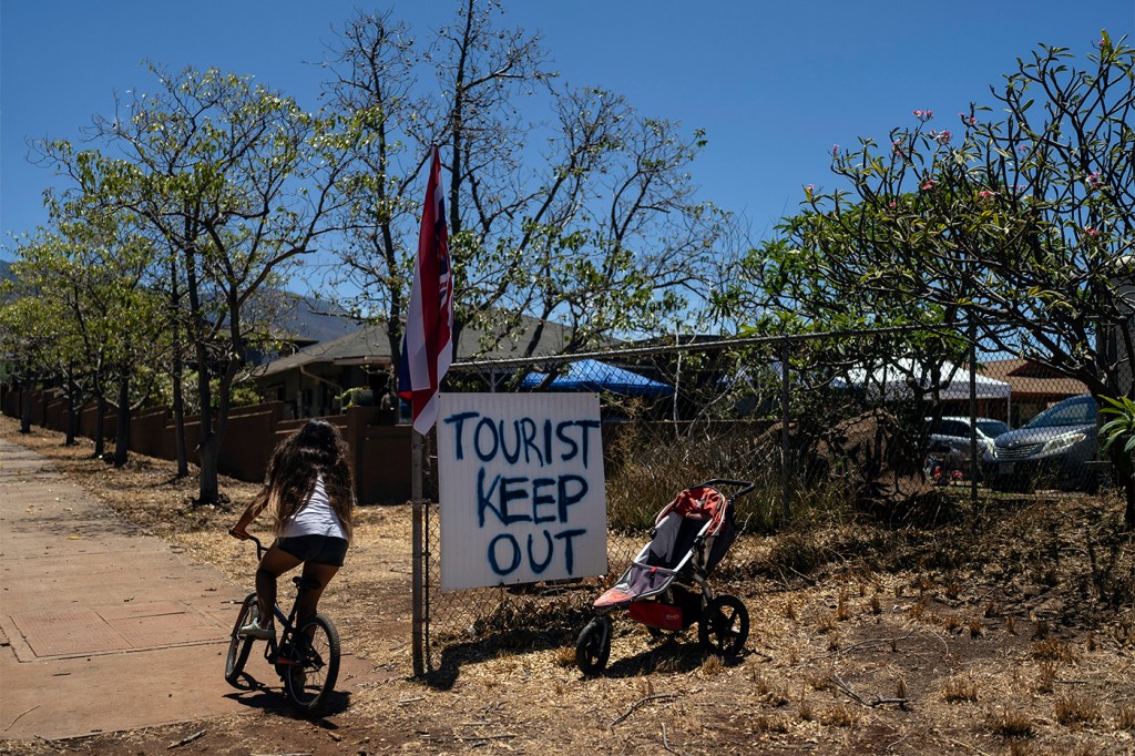 A girl riding her bike past a sign in Maui that says "Tourist Keep Out".