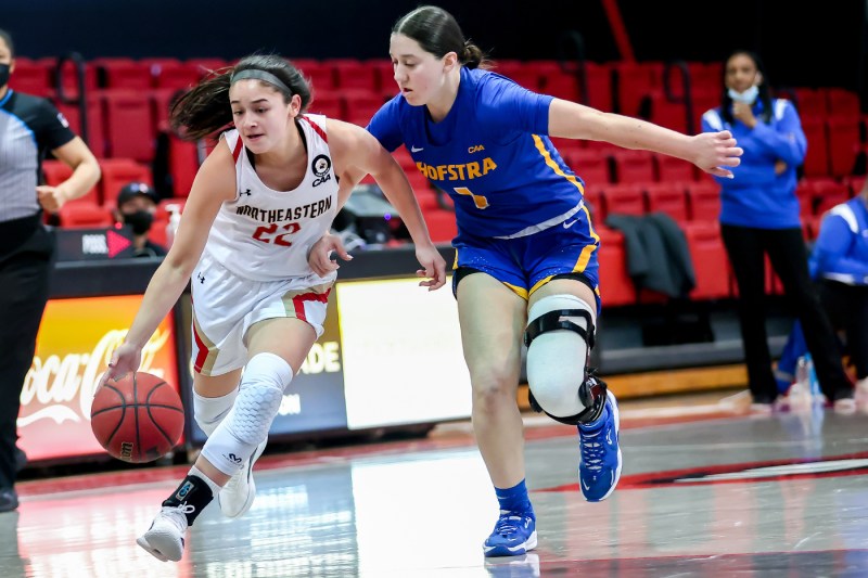 Two womens basketball players running down the court, one dribbling the ball 