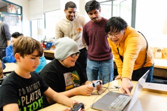 Students huddled around a laptop working on game design together.