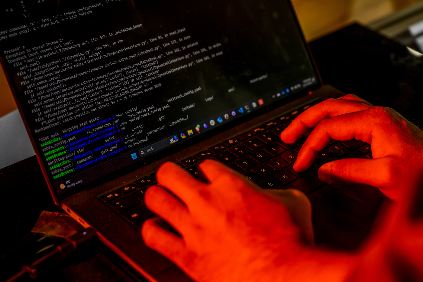 Person typing code on a laptop in a room with red lighting. 