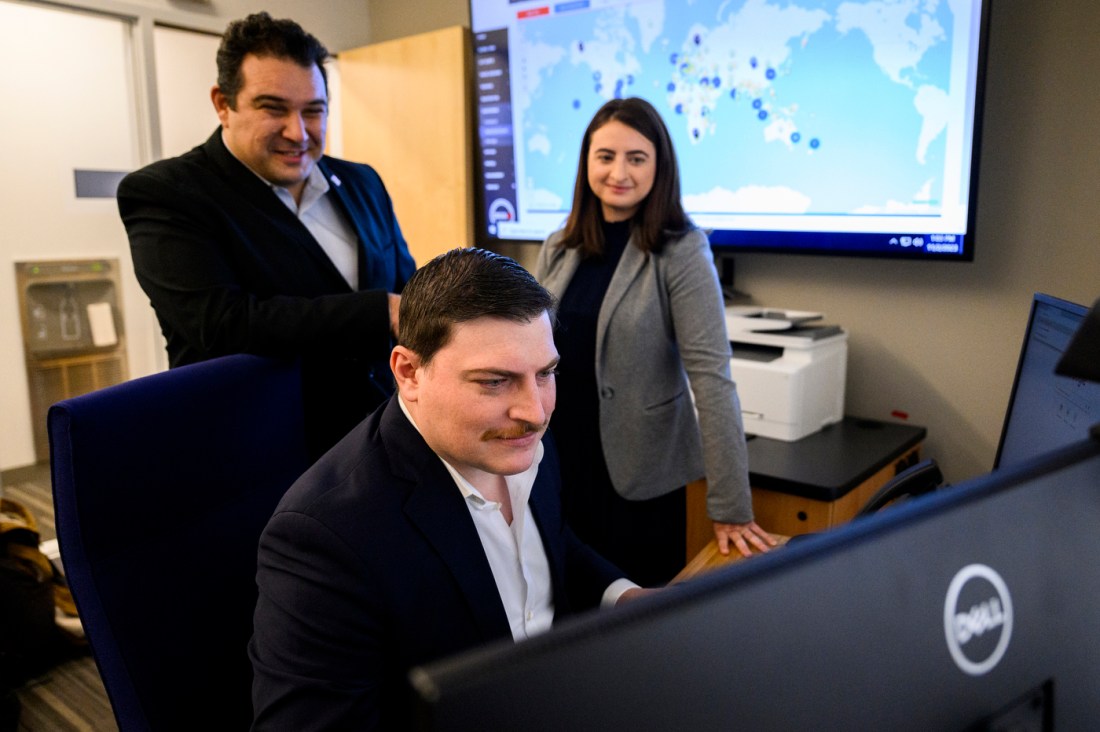 Khushal Safi working on a desktop computer while Alyssa Berg and JJ Cappa look over his shoulder.