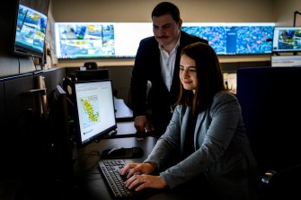 Alyssa Berg and JJ Cappa working on a laptop in an office with many screens.