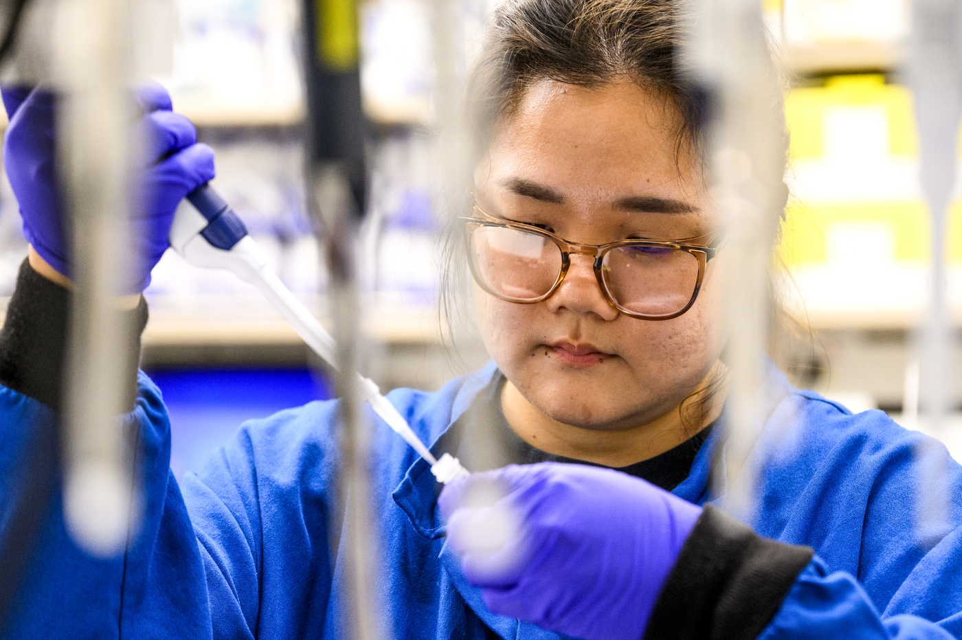A person wearing a laboratory coat and gloves holds a test tube. 