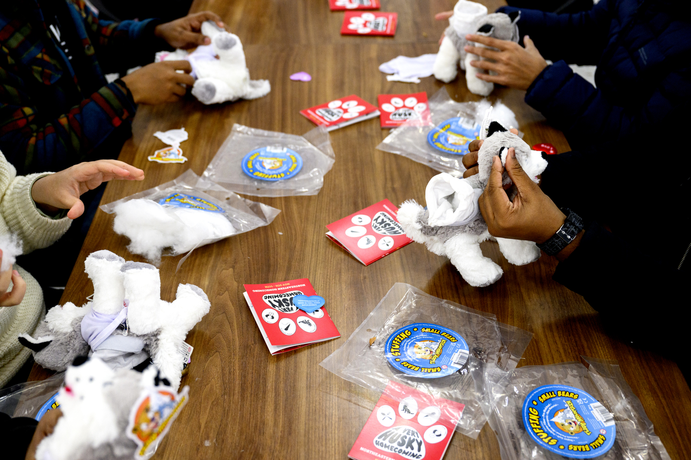 People sit around a table, stuffing husky stuffed animals.