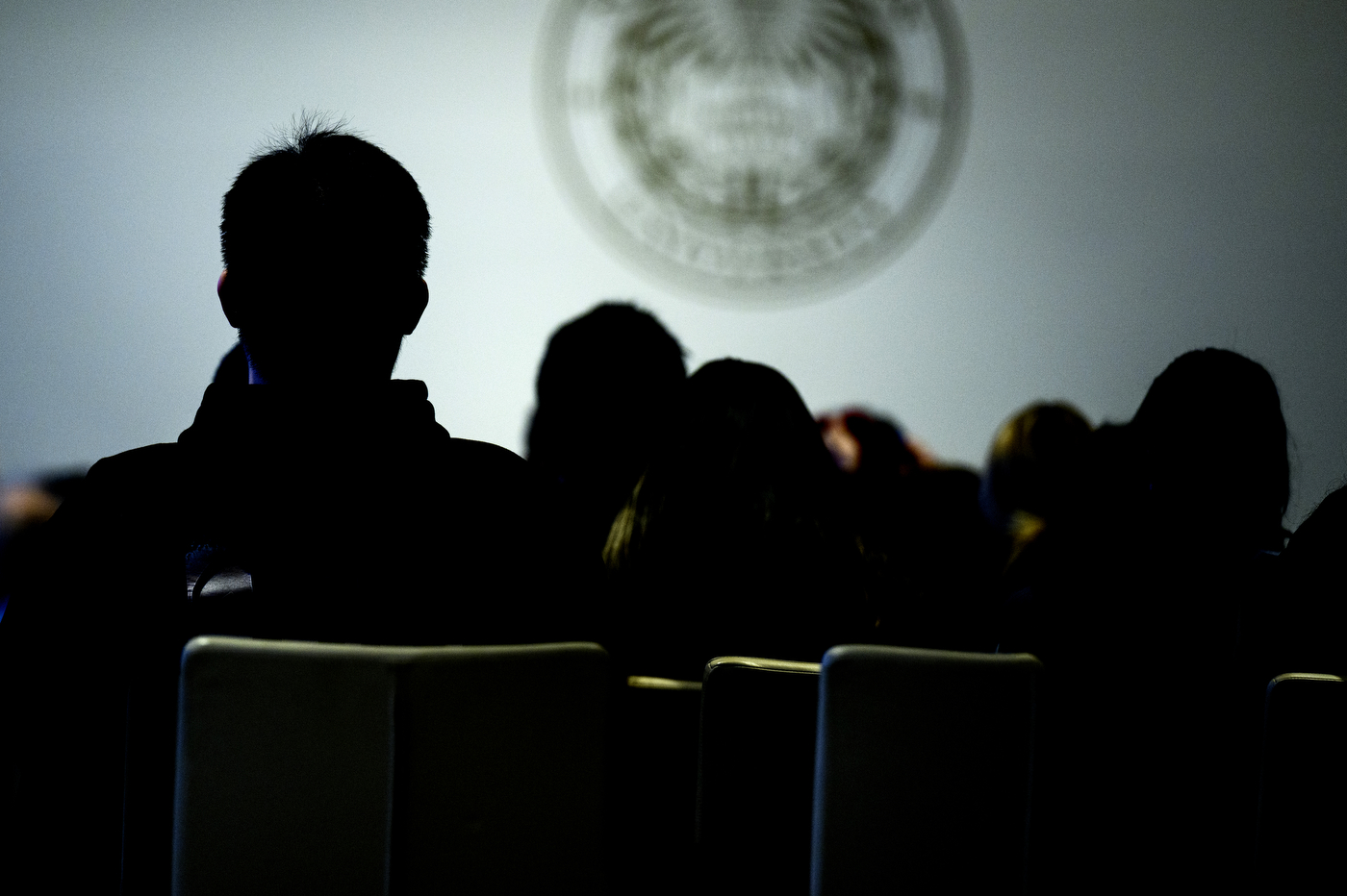 Silhouette of audience members sitting in front of a brightly lit stage.