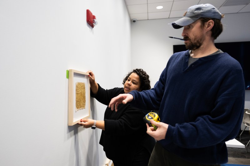 Two people installing pieces art exhibit pieces on a wall.