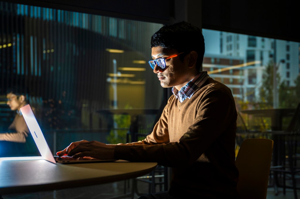 Basu Roy sitting at a laptop in a dark room.