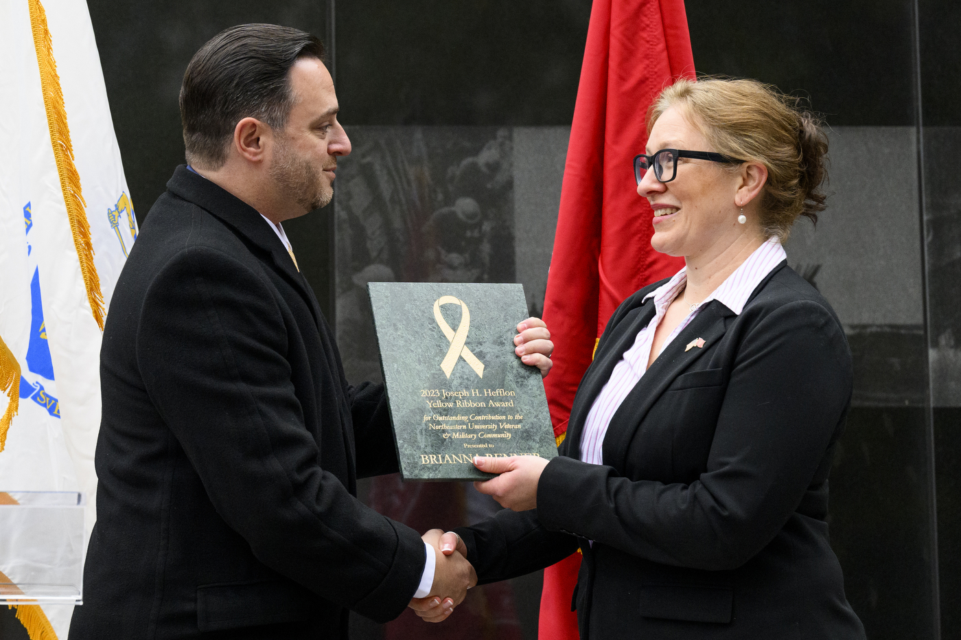 A person presenting an award to another person while shaking their hand.