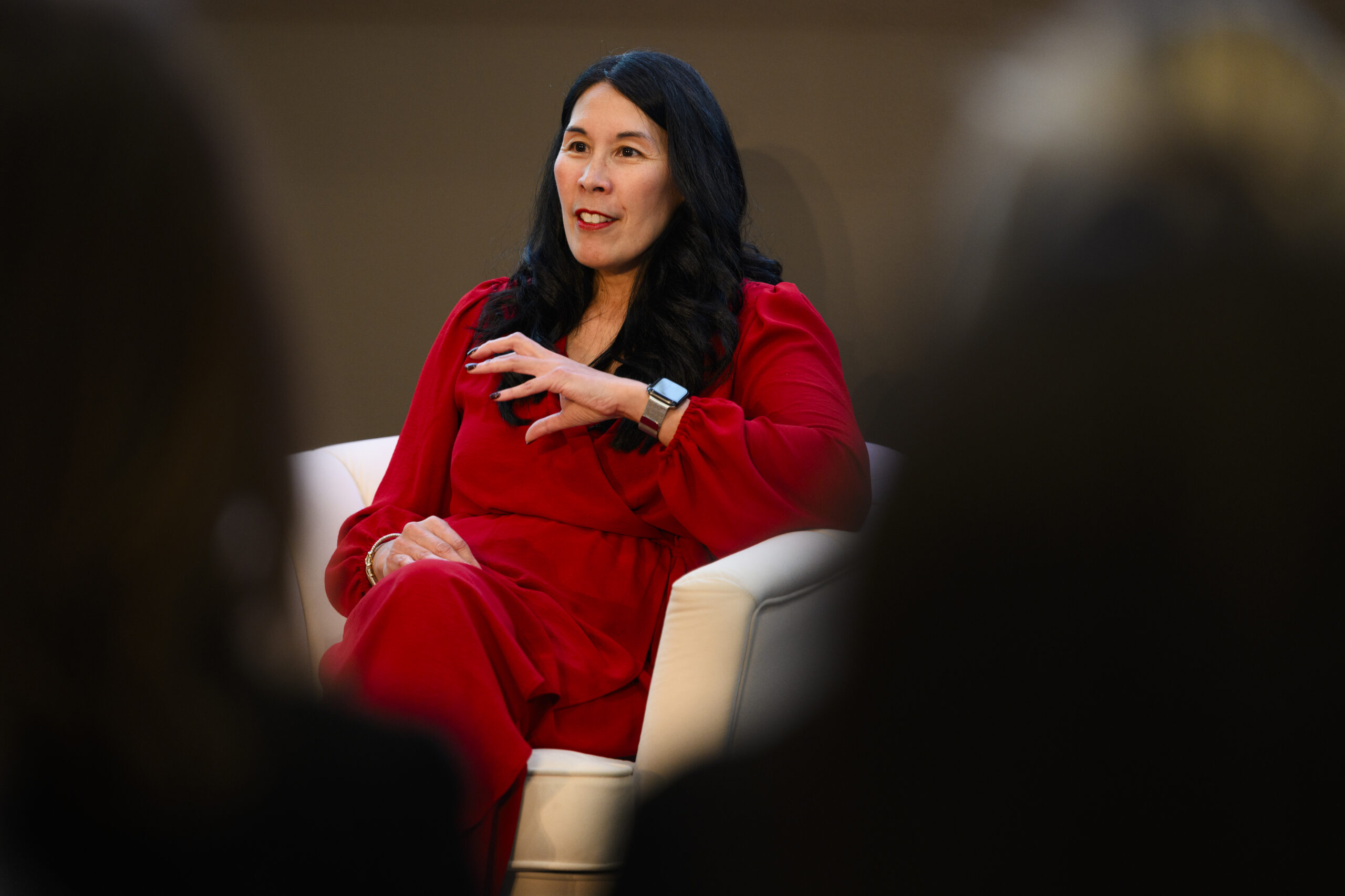 Betty Francisco sitting in a white chair wearing red speaking at the Women Who Empower summit.