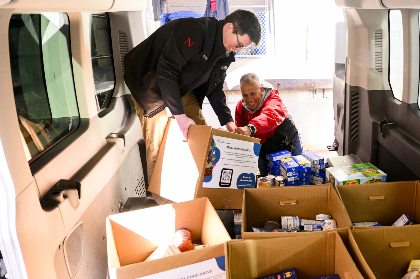 Two members of the Northeastern community loading boxes of food donations into a truck. 