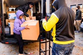 People unloading boxes of food donations from a truck onto a dolly.