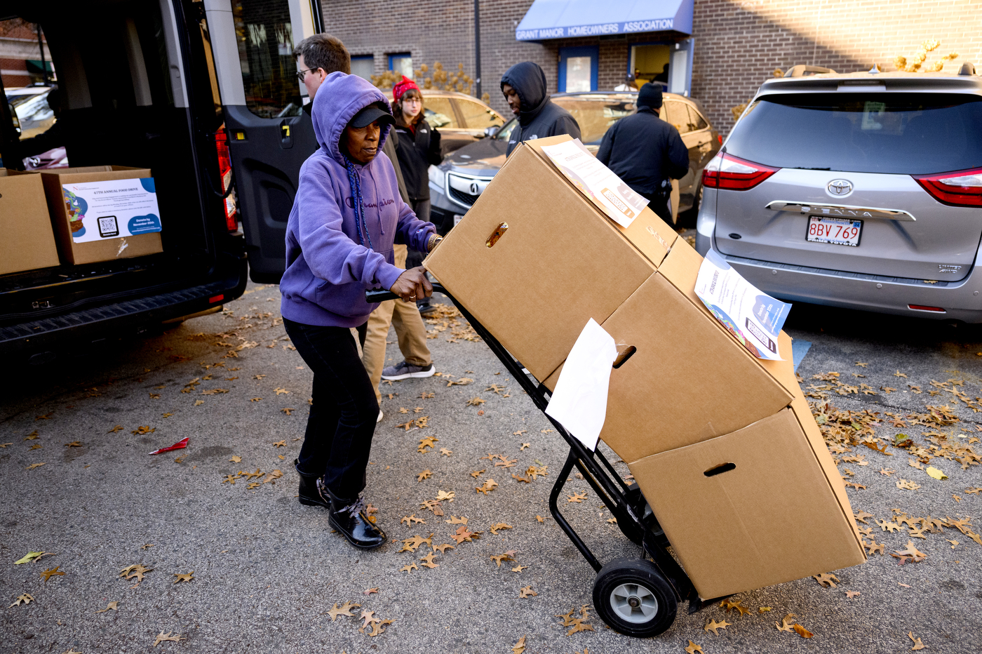 Person using a dolly to wheel three stacked boxes of food donations away from a truck. 