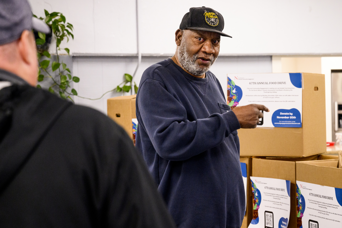 Person gesturing to a box of food donations. 