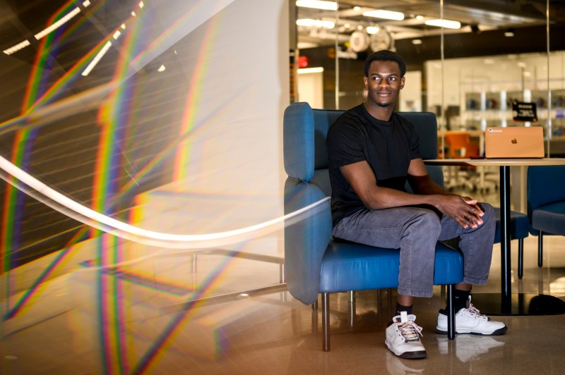 David Alade sitting on a blue curved chair next to a table.